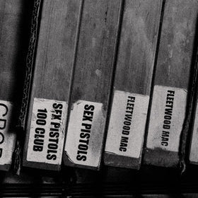 Black and white close-up of several book spines labeled with phrases such as 'SEX PISTOLS 100 CLUB', 'SEX PISTOLS', 'FLEETWOOD MAC'