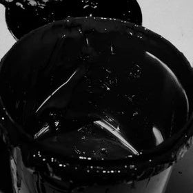 A close-up of a glossy black paint or ink container with a brush resting inside, photographed in monochrome against a light background.