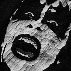 Black and white close-up of a graphic print featuring a stylized screaming face on a dark fabric background.