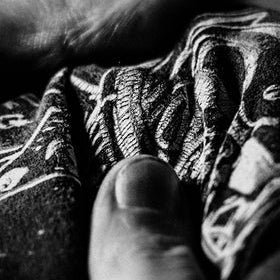 Black and white close-up of a hand holding and smoothing a patterned fabric with a detailed dragon or creature design.